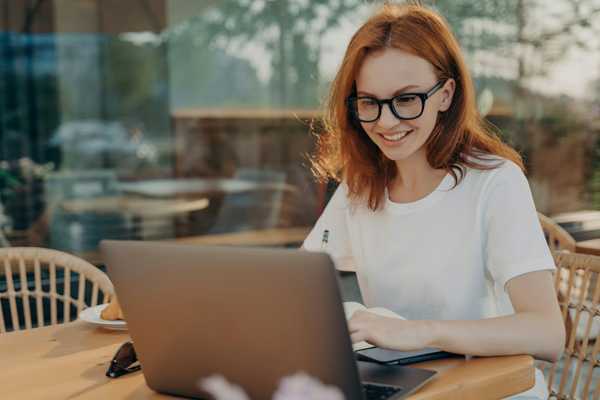 Joyful young woman enjoying an online meeting with friends at a cafe, engaging with her laptop